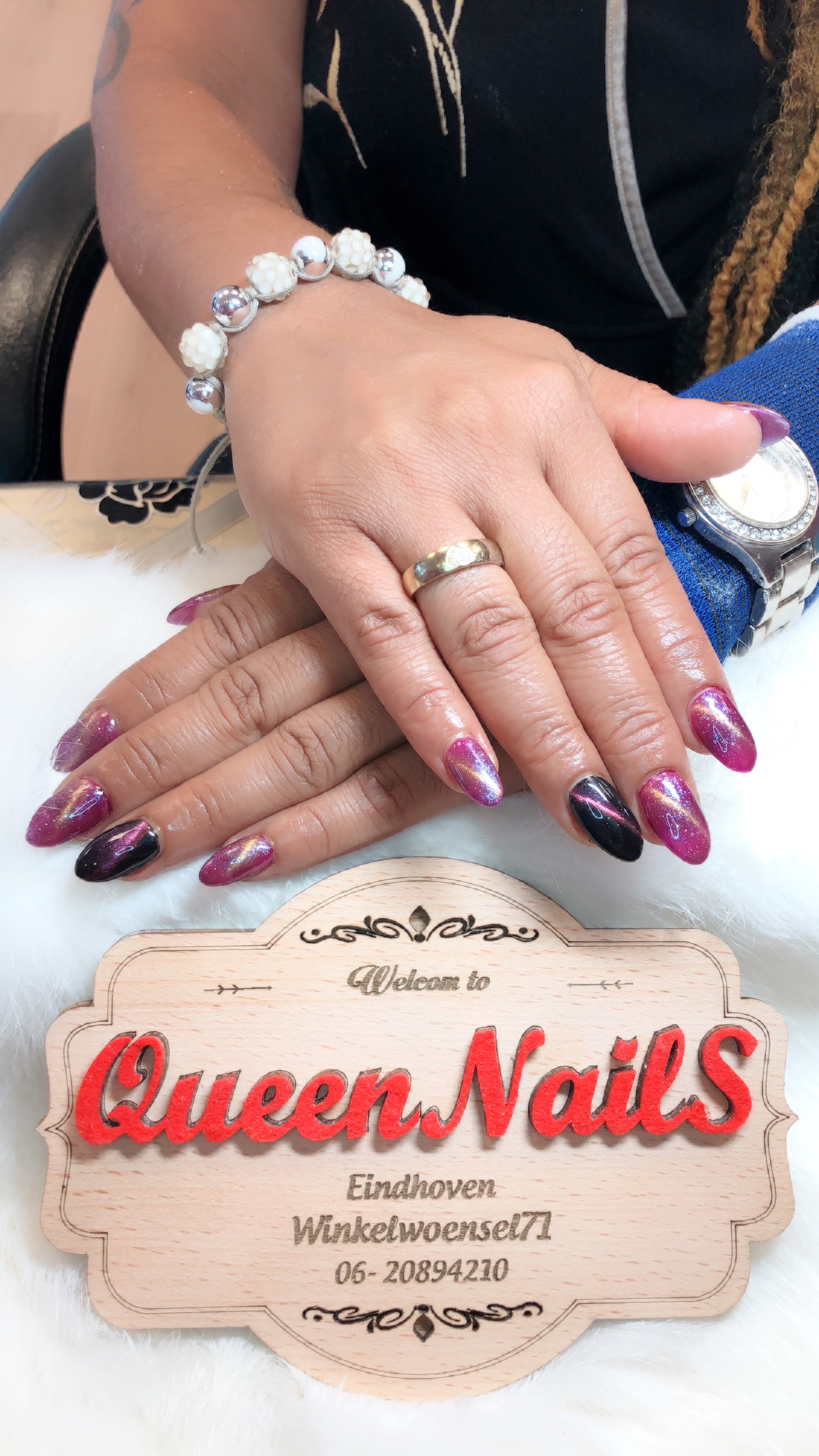 Lange paarsroze nagels boven een Queen Nails-displaybord