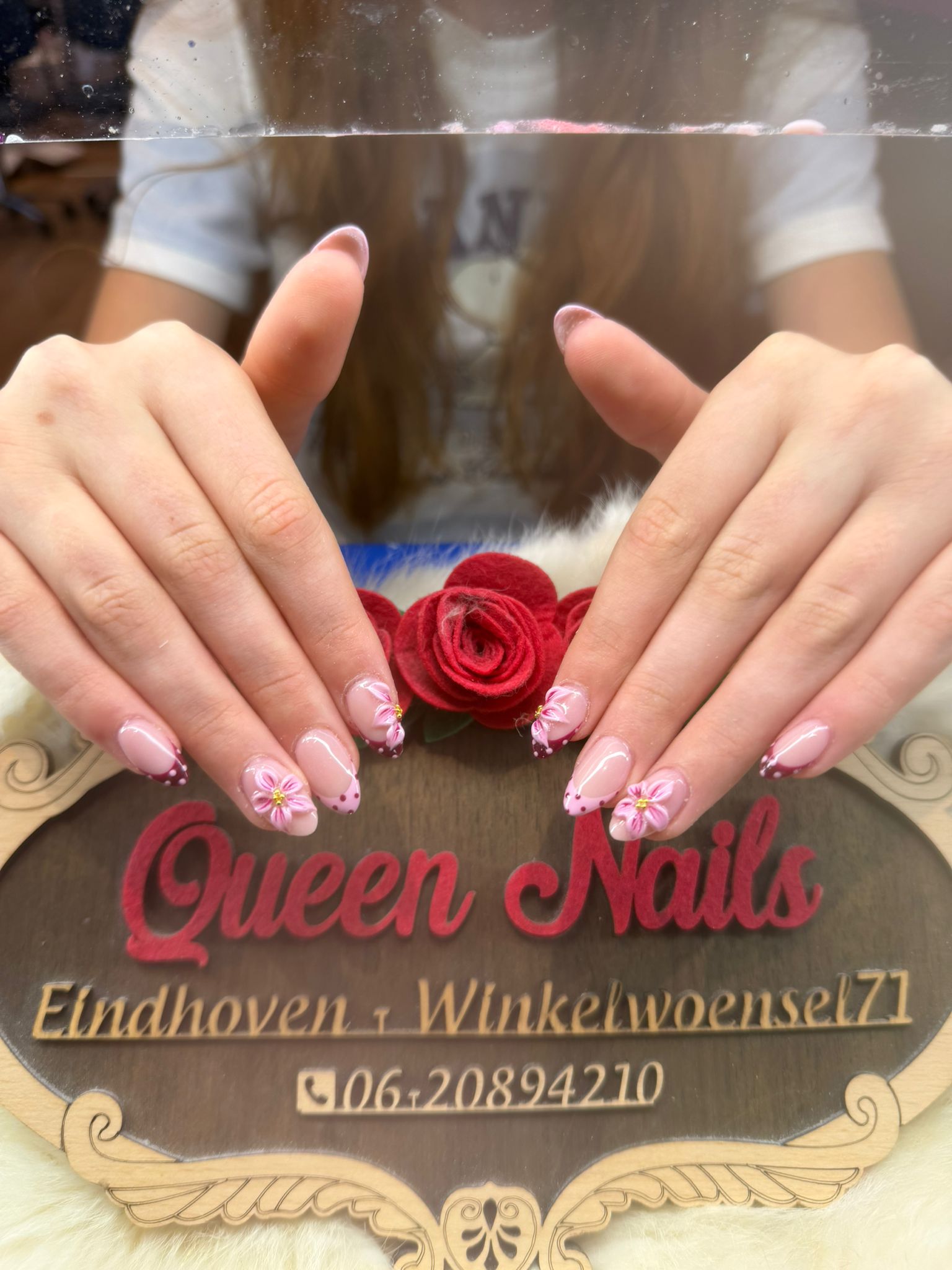 Roze nagels met bloemendecoratie en Queen Nails-bord